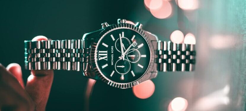Silver Michael Kors wristwatch with Roman numerals and elegant design, highlighted by bokeh lights.